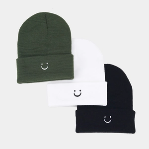 Detailed view of high-density knit beanies in dark green, white, and black with smiley embroidery