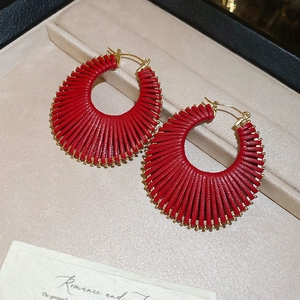 Détail de boucles d'oreilles créoles tressées rouges avec accents dorés dans un écrin beige