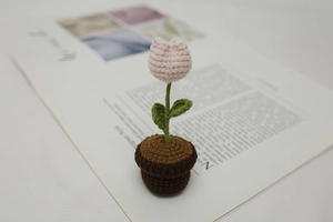 Detailed view of a handmade pink crochet tulip in a brown knitted pot on a book