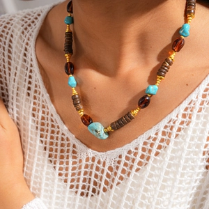 Detail of ethnic beaded necklace with turquoise and amber acrylic stones on white knitwear