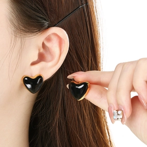 Detail of heart-shaped enamel earrings in black and gold worn on model ear