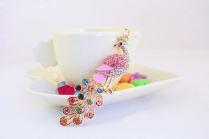 Close-up of golden peacock keychain with colorful rhinestones on a white coffee cup