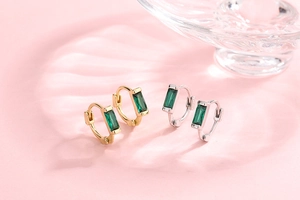 Macro shot of gold and silver huggie earrings with emerald green rectangular gemstones