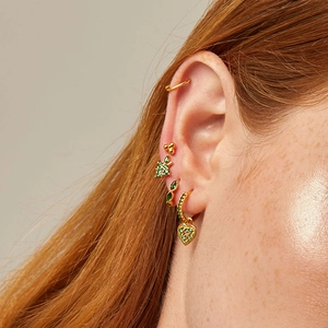 Close-up of gold ear cuff set with green zircon stones worn in a multi-piercing style