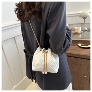 Close-up of white quilted bucket bag featuring pearl drawstring and metal chain strap
