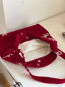 Detail of red corduroy shoulder bag showing bow embroidery and magnetic snap closure