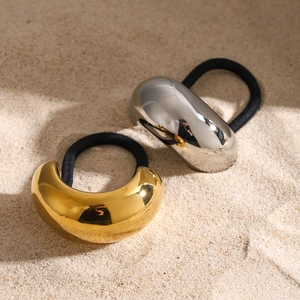 Golden and silver stainless steel hair ties with oval metal charms on sand background