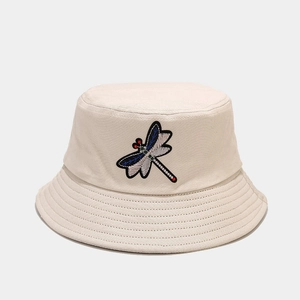 Close-up of a beige canvas bucket hat featuring detailed dragonfly embroidery on the crown