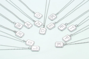Silver initial pendant necklaces with crystal pavé alphabets on light blue backdrop