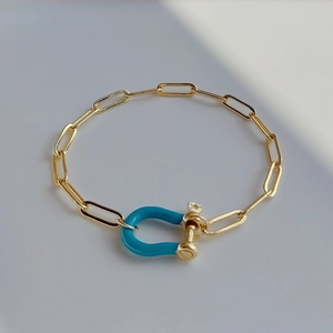 Detail of golden paperclip chain bracelet featuring a turquoise enamel horseshoe clasp