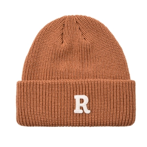 Dettaglio del berretto in maglia color caramello con ricamo R bianco e trama spessa