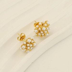 Detailed close-up of golden 18k pearl cluster stud earrings on a white textured stand