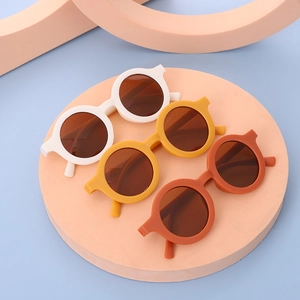 Trio of round frame kids sunglasses in cream, yellow, and orange on a soft display