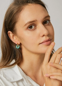 Close-up of golden hoop earrings featuring a turquoise marble bead worn by a model