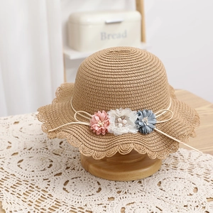 Dettaglio macro del cappello di paglia con tre fiori in tessuto, perle e bordo ondulato
