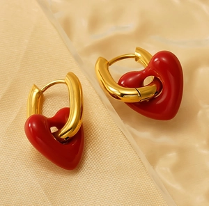 Detail of gold U-shaped hoop earrings with red enamel heart pendant on textured background