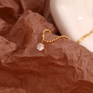 Vista macro di una collana a catena a sfere placcata oro 18K con un singolo zircone bianco