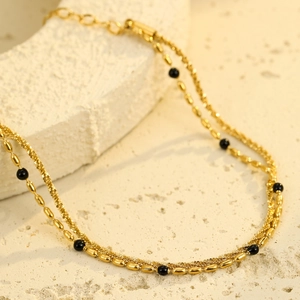 Macro detail of 18K gold-plated double-layer chain bracelet with elegant black beads