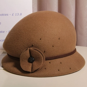 Dettaglio cappello cloche in lana con fiore caramello e accenti di perle dorate