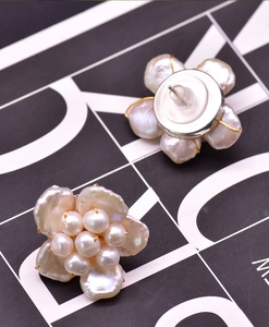 Detail view of flower-shaped pearl earrings with gold base, silver pins and clear backings