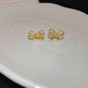 Detailed view of polished golden bow stud earrings placed on white ceramic plate
