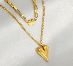Detail view of double-layered gold heart necklace with puffy heart pendant on satin