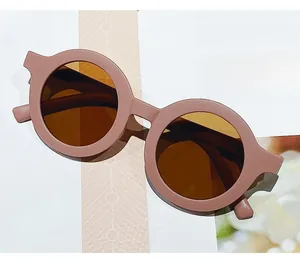 Detail view of round matte pink kids sunglasses with brown lenses on a magazine backdrop