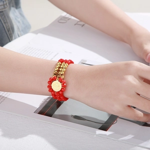 Close-up of a red glass beaded bracelet with a gold Saint Benedict coin charm on a model