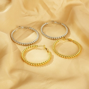 Macro detail of twisted textured hoop earrings in gold and silver on yellow satin