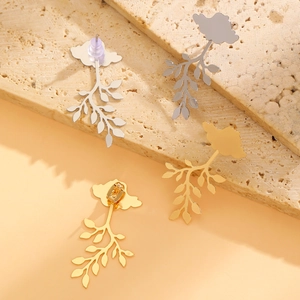 Detailed view of leaf-shaped gold and silver earrings on a beige travertine stone
