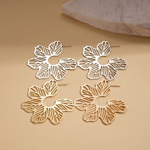 Minimalist metallic hollow flower stud earrings in gold and silver finishes on a warm base