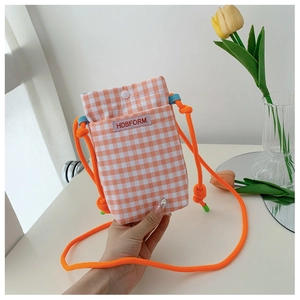Detail view of orange plaid crossbody phone bag with knot strap and tulip background