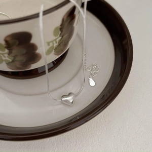 Detail of silver heart pendant with matte brushed finish on vintage ceramic saucer
