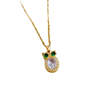 Elegant gold owl necklace featuring clear oval gemstone and green jewel eyes on white base
