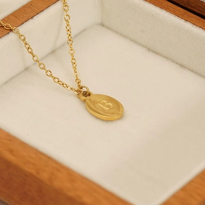 Detailed close-up of golden stainless steel oval pendant with letter B in a jewelry box
