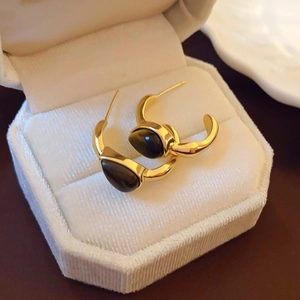 Macro shot of vintage C-shaped gold metal earrings featuring oval tiger eye stone in a box