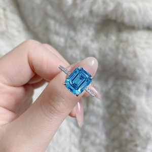 Macro shot of an emerald-cut aquamarine ring with side diamonds on a white faux fur background