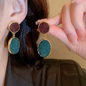 Close-up of vintage gold earrings with deep red and dark green textured resin inlays