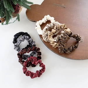 8-pack large leather-textured scrunchies in neutral colors on a bear wooden tray