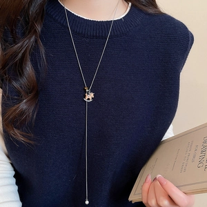 Silver necklace with wooden horse pendant and pearl on a model wearing blue knitwear