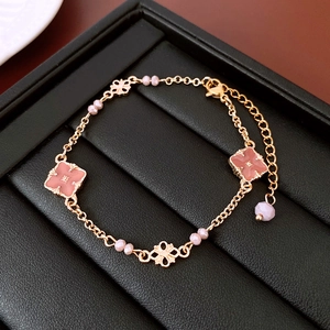 Dettaglio dei ciondoli a fiori rosa e del bracciale dorato con perline e chiusura a moschettone