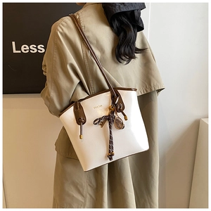 Détail du sac seau en cuir blanc avec nœud tressé marron et breloque raquette