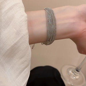 Detail of layered silver metal chain bracelet worn on wrist with adjustable clasp