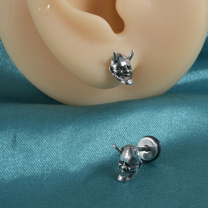Vue macro détaillée du clou d'oreille masque de démon en argent sur satin bleu