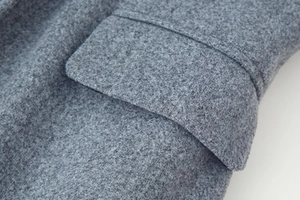 Detail view of the gray wool coat showing fabric texture, pocket flap, and precise stitching