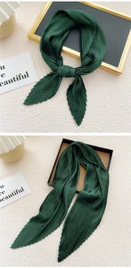 Macro shot of dark green pleated silk scarf showing vertical pleats and satin luster texture