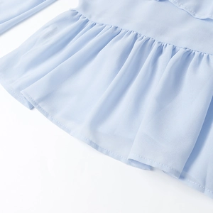 Dettaglio di balze azzurre su camicetta di chiffon con trama plissettata delicata