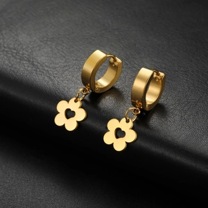 Detail view of golden flower earrings with heart cutouts on a black leather background