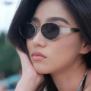 Close-up of retro oval metal sunglasses with silver frames and dark grey lenses on model