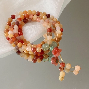 Detail eines mehrlagigen Perlenarmbands mit rotem Blumenanhänger und Quasten im Retro-Stil